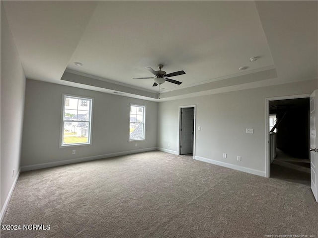 empty room with light carpet, ornamental molding, ceiling fan, and a raised ceiling