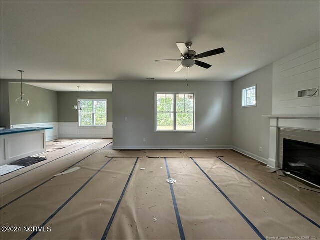 unfurnished living room featuring ceiling fan with notable chandelier and plenty of natural light