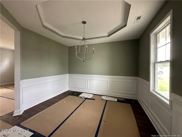 unfurnished dining area with dark wood-type flooring, a notable chandelier, ornamental molding, and a tray ceiling