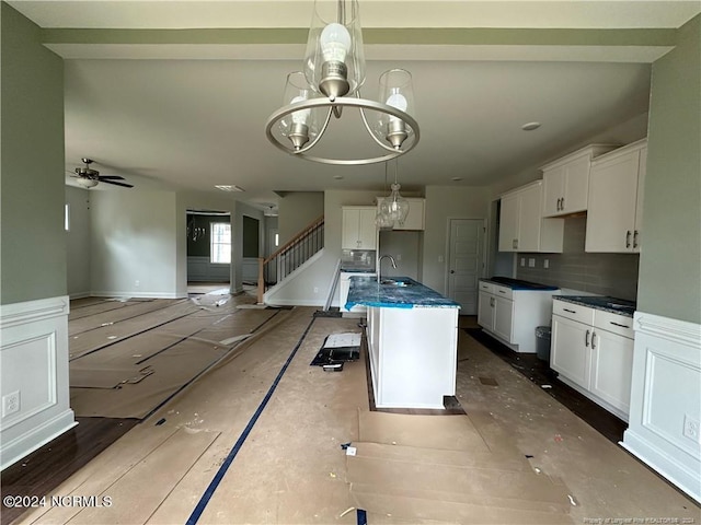 kitchen featuring tasteful backsplash, sink, an island with sink, white cabinetry, and decorative light fixtures