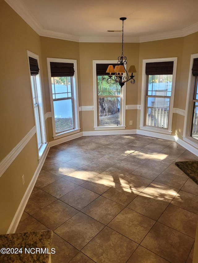 unfurnished dining area featuring dark tile patterned flooring, ornamental molding, and an inviting chandelier