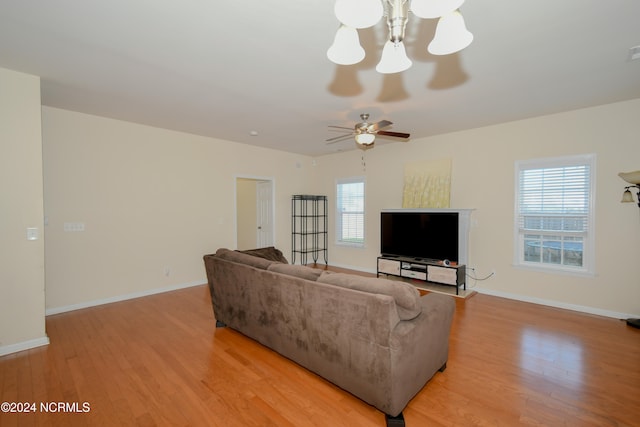 living room with a wealth of natural light, ceiling fan with notable chandelier, and light hardwood / wood-style floors