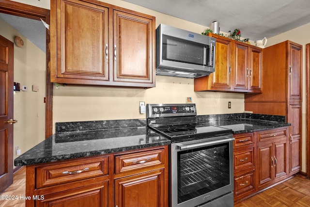 kitchen featuring stainless steel appliances, dark stone countertops, a textured ceiling, and light parquet flooring