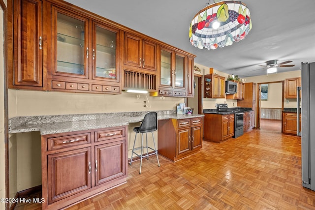 kitchen featuring light parquet floors, light stone counters, built in desk, stainless steel appliances, and ceiling fan