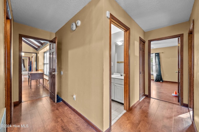 corridor with light wood-type flooring, a textured ceiling, sink, and vaulted ceiling