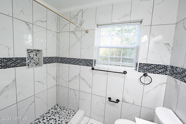 bathroom with a tile shower, toilet, and ornamental molding