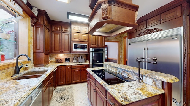 kitchen with light tile patterned flooring, island range hood, sink, built in appliances, and light stone countertops