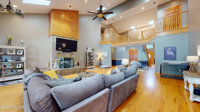 living room featuring a fireplace, a skylight, wood-type flooring, a high ceiling, and ceiling fan