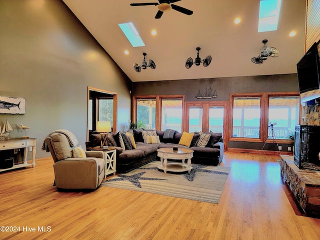 living room featuring a skylight, high vaulted ceiling, light hardwood / wood-style floors, and ceiling fan