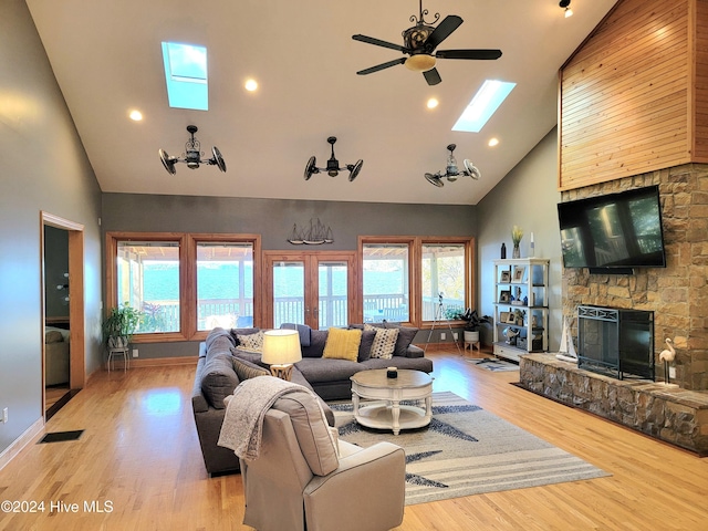 living room with ceiling fan, a skylight, high vaulted ceiling, a fireplace, and light wood-type flooring