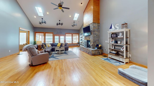 living room featuring hardwood / wood-style flooring, a skylight, high vaulted ceiling, and a stone fireplace