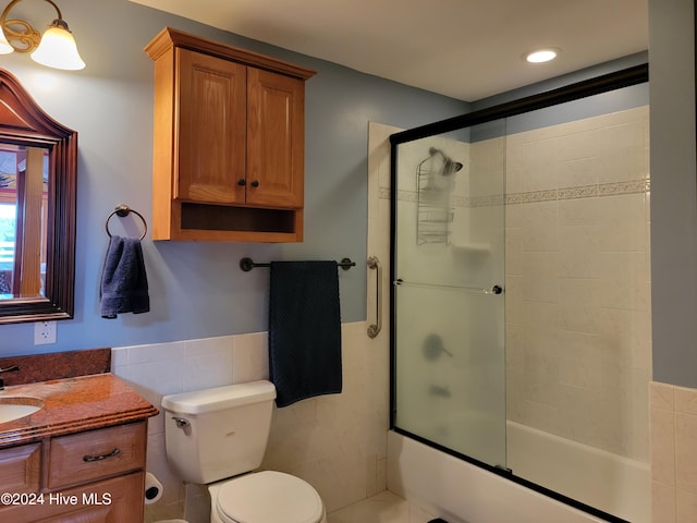 full bathroom with tile walls, vanity, bath / shower combo with glass door, and toilet