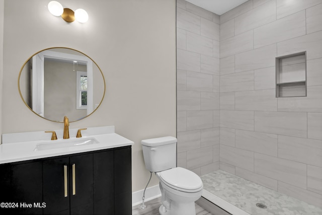 bathroom with tiled shower, hardwood / wood-style floors, vanity, and toilet