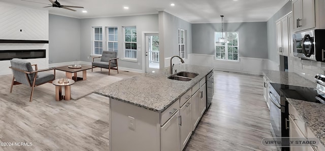 kitchen featuring light stone counters, an island with sink, appliances with stainless steel finishes, sink, and decorative light fixtures