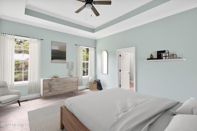 bedroom featuring ceiling fan, a raised ceiling, ornamental molding, and light hardwood / wood-style flooring