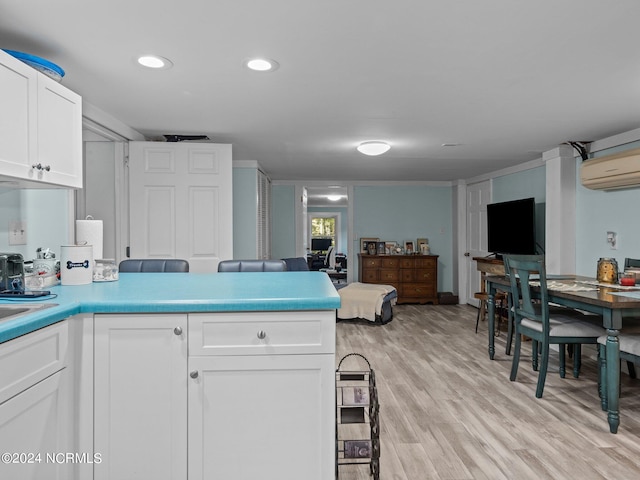 kitchen with a wall mounted air conditioner, light hardwood / wood-style flooring, and white cabinets