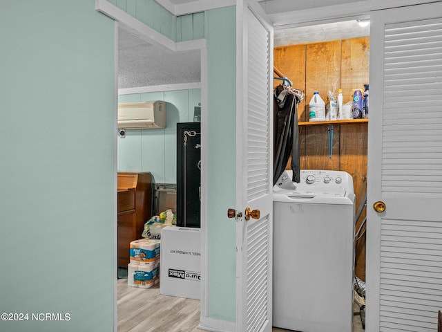 clothes washing area featuring washer / dryer, a wall unit AC, a textured ceiling, and light hardwood / wood-style flooring