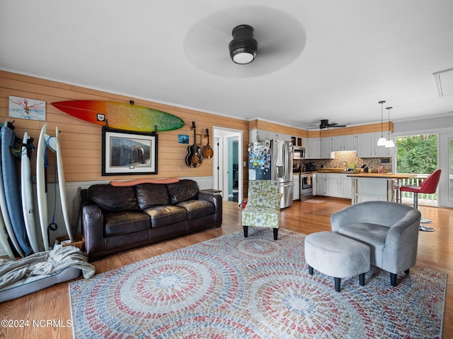 living room with sink, wooden walls, light wood-type flooring, and ceiling fan