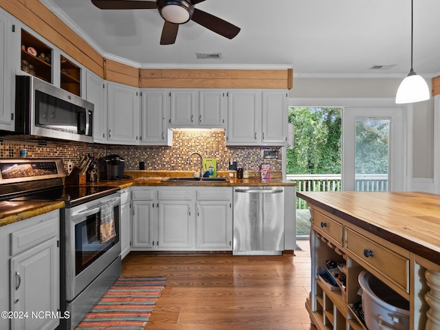 kitchen with hanging light fixtures, stainless steel appliances, crown molding, sink, and white cabinets