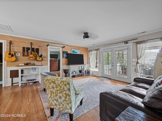 living room with light hardwood / wood-style floors, french doors, wood walls, and ceiling fan