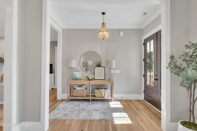 entryway with light hardwood / wood-style floors, ornamental molding, and a chandelier