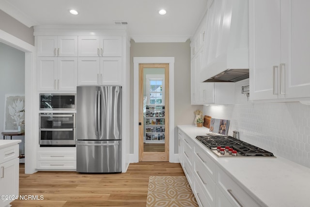 kitchen with appliances with stainless steel finishes, light hardwood / wood-style floors, custom exhaust hood, white cabinets, and decorative backsplash