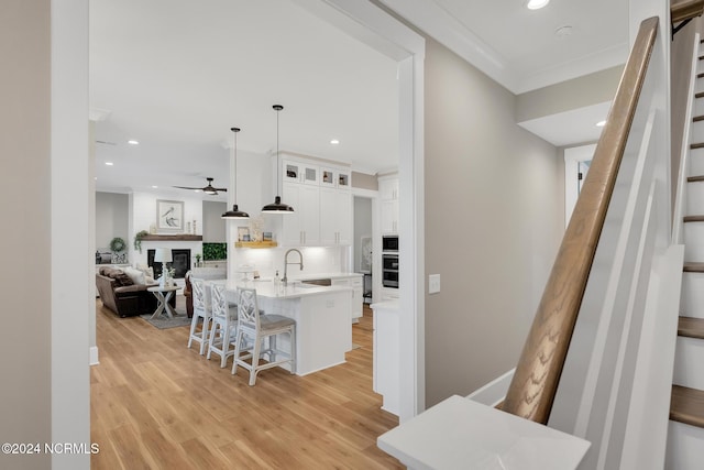 kitchen with an island with sink, a breakfast bar area, white cabinetry, pendant lighting, and sink