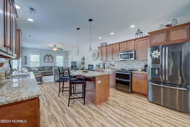 kitchen featuring hanging light fixtures, a center island, light stone counters, and stainless steel appliances