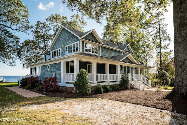 view of front facade with covered porch, a front lawn, and a water view