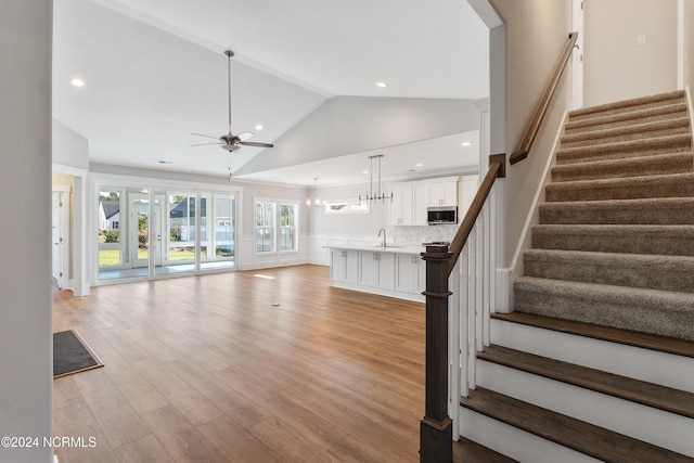 unfurnished living room featuring light hardwood / wood-style floors, high vaulted ceiling, sink, and ceiling fan with notable chandelier