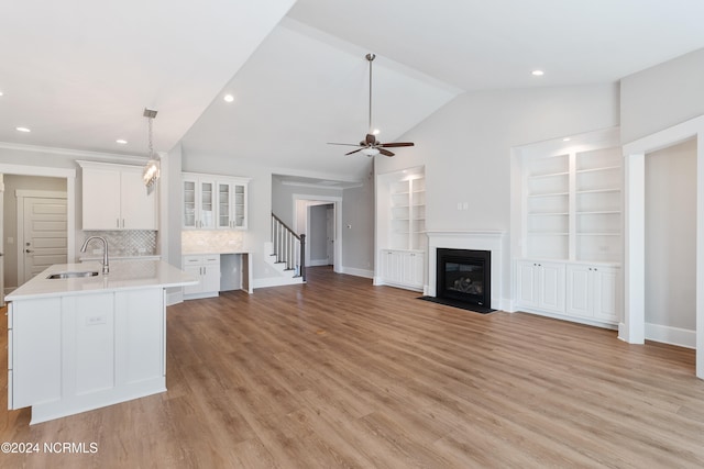 kitchen with lofted ceiling, sink, decorative light fixtures, white cabinetry, and light hardwood / wood-style floors