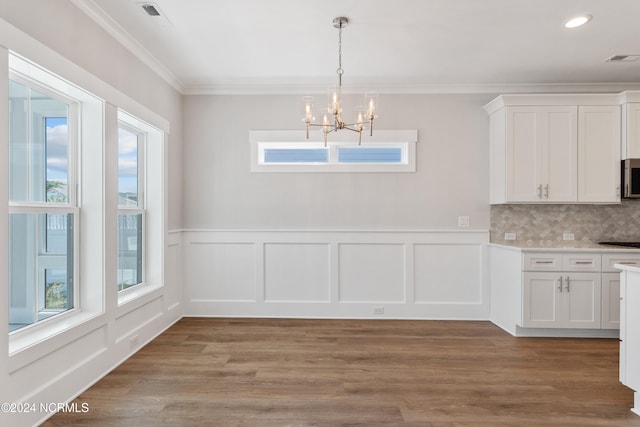 unfurnished dining area featuring light hardwood / wood-style floors, ornamental molding, an inviting chandelier, and plenty of natural light