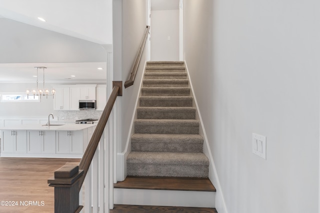 staircase with hardwood / wood-style floors, sink, vaulted ceiling, and an inviting chandelier