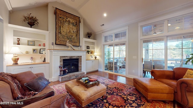 living room with a brick fireplace, hardwood / wood-style floors, built in features, and high vaulted ceiling