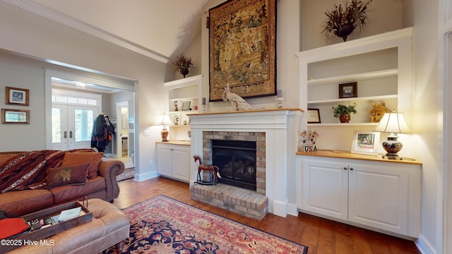 living room featuring lofted ceiling, light hardwood / wood-style floors, a brick fireplace, built in shelves, and french doors