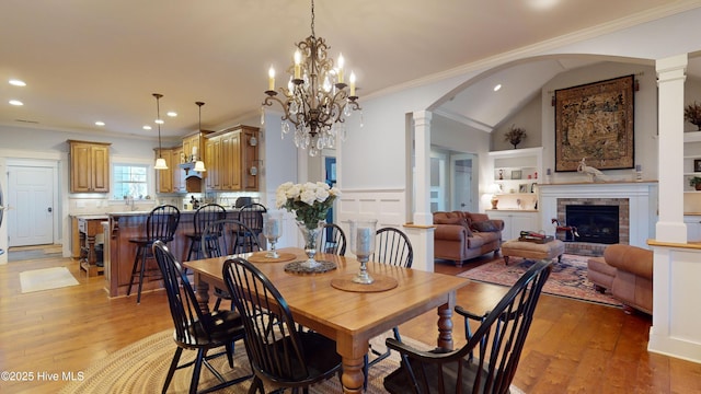 dining room featuring ornamental molding, decorative columns, a brick fireplace, and light wood-type flooring