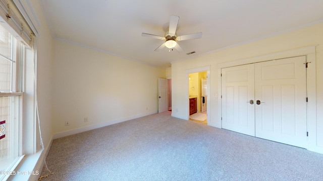 unfurnished bedroom featuring ensuite bathroom, ornamental molding, light colored carpet, ceiling fan, and a closet