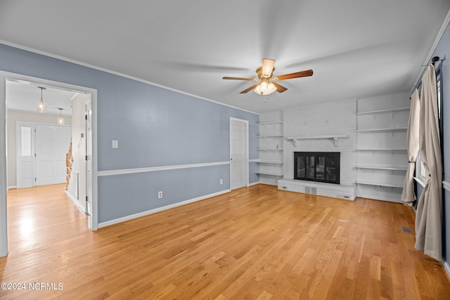 unfurnished living room featuring ornamental molding, a brick fireplace, light wood-type flooring, built in shelves, and ceiling fan