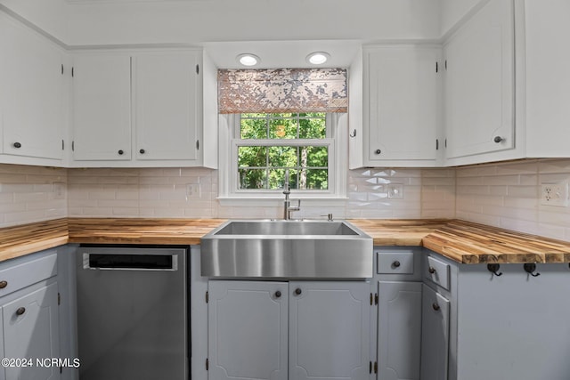 kitchen with white cabinets, backsplash, wood counters, stainless steel dishwasher, and sink