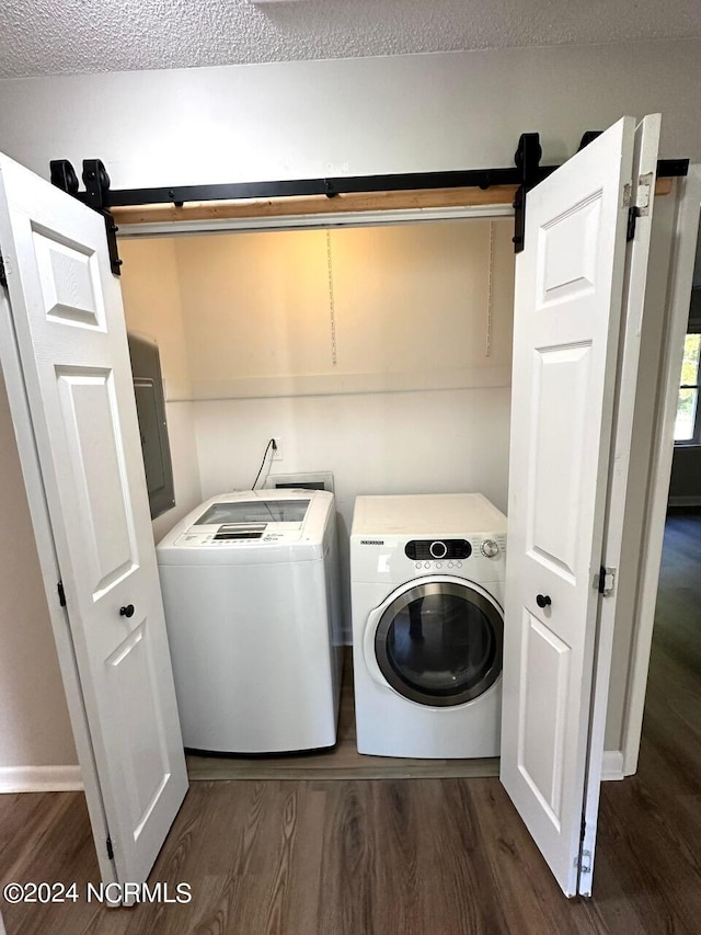 clothes washing area featuring washer and clothes dryer, dark wood-type flooring, a barn door, electric panel, and a textured ceiling