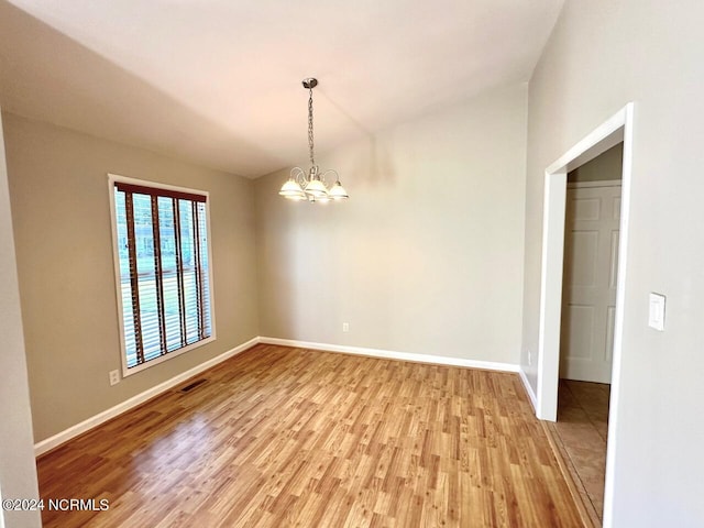 spare room featuring a notable chandelier, hardwood / wood-style floors, and vaulted ceiling