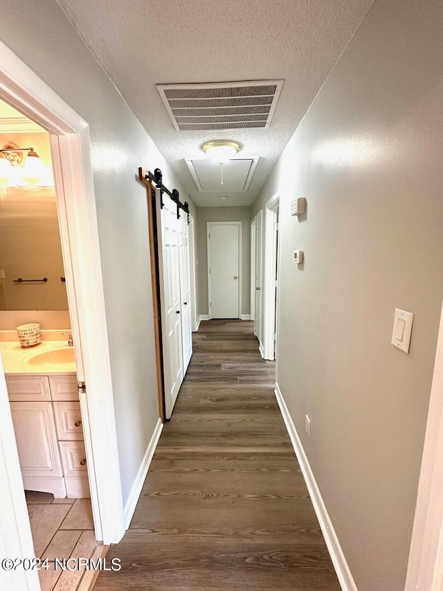 corridor featuring sink, a barn door, dark hardwood / wood-style floors, and a textured ceiling