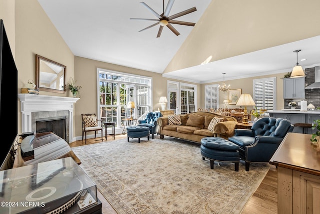 living room featuring a tile fireplace, ceiling fan with notable chandelier, high vaulted ceiling, and light hardwood / wood-style flooring