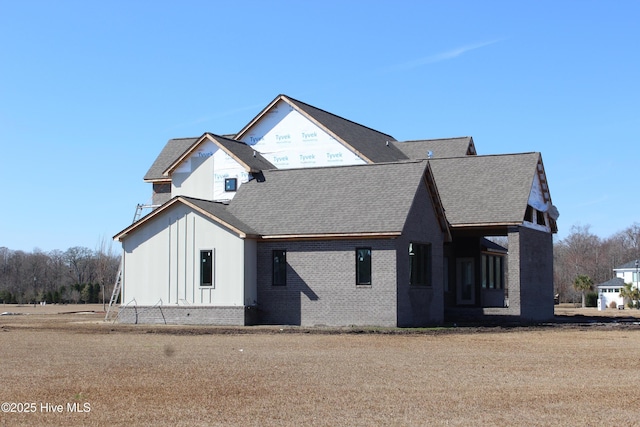 view of front of house featuring a shingled roof, board and batten siding, and brick siding