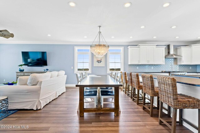 kitchen featuring dark wood-type flooring, wall chimney range hood, hanging light fixtures, and white cabinets