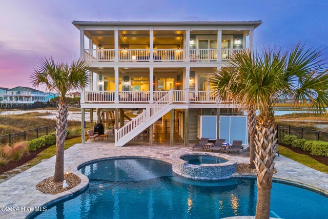 back house at dusk with a pool with hot tub, a patio, and a balcony