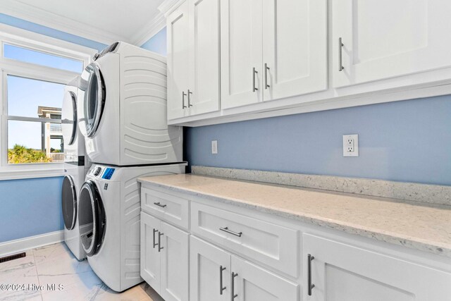 laundry area with cabinets, crown molding, and stacked washer / drying machine