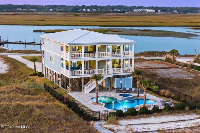 back house at dusk with a pool with hot tub, a balcony, a patio, and a water view