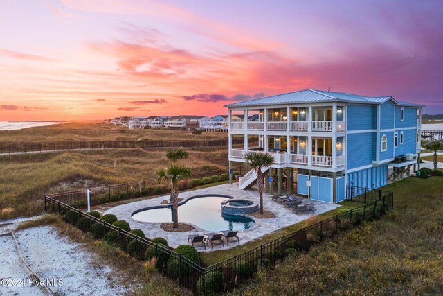 back house at dusk featuring a balcony, a patio, and a pool with hot tub