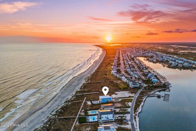 aerial view at dusk featuring a water view and a view of the beach